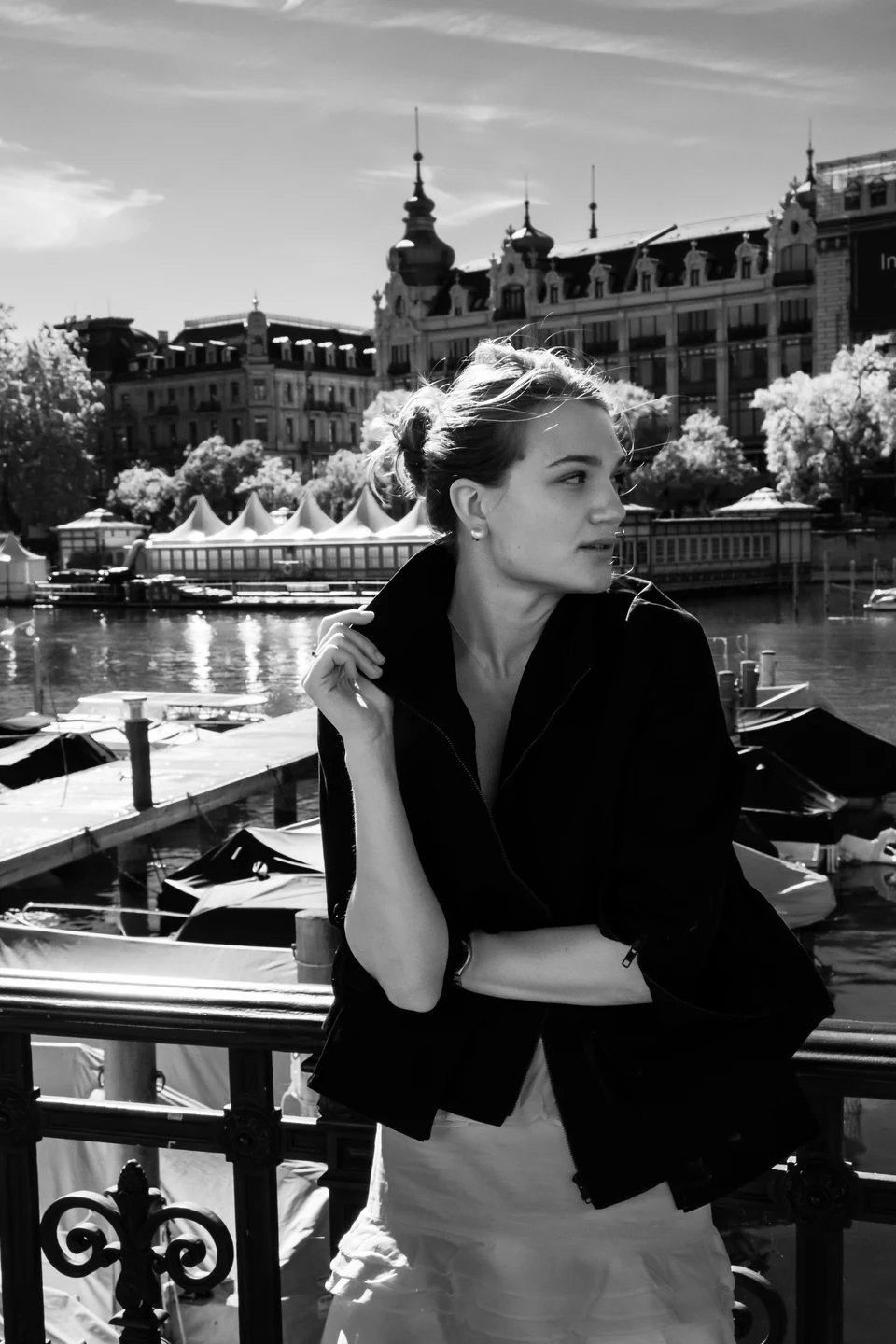 Monochrome portrait beside a riverside railing with city buildings behind.