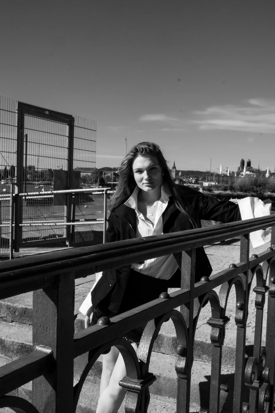 Monochrome seated portrait on a bridge with city rooftops behind.