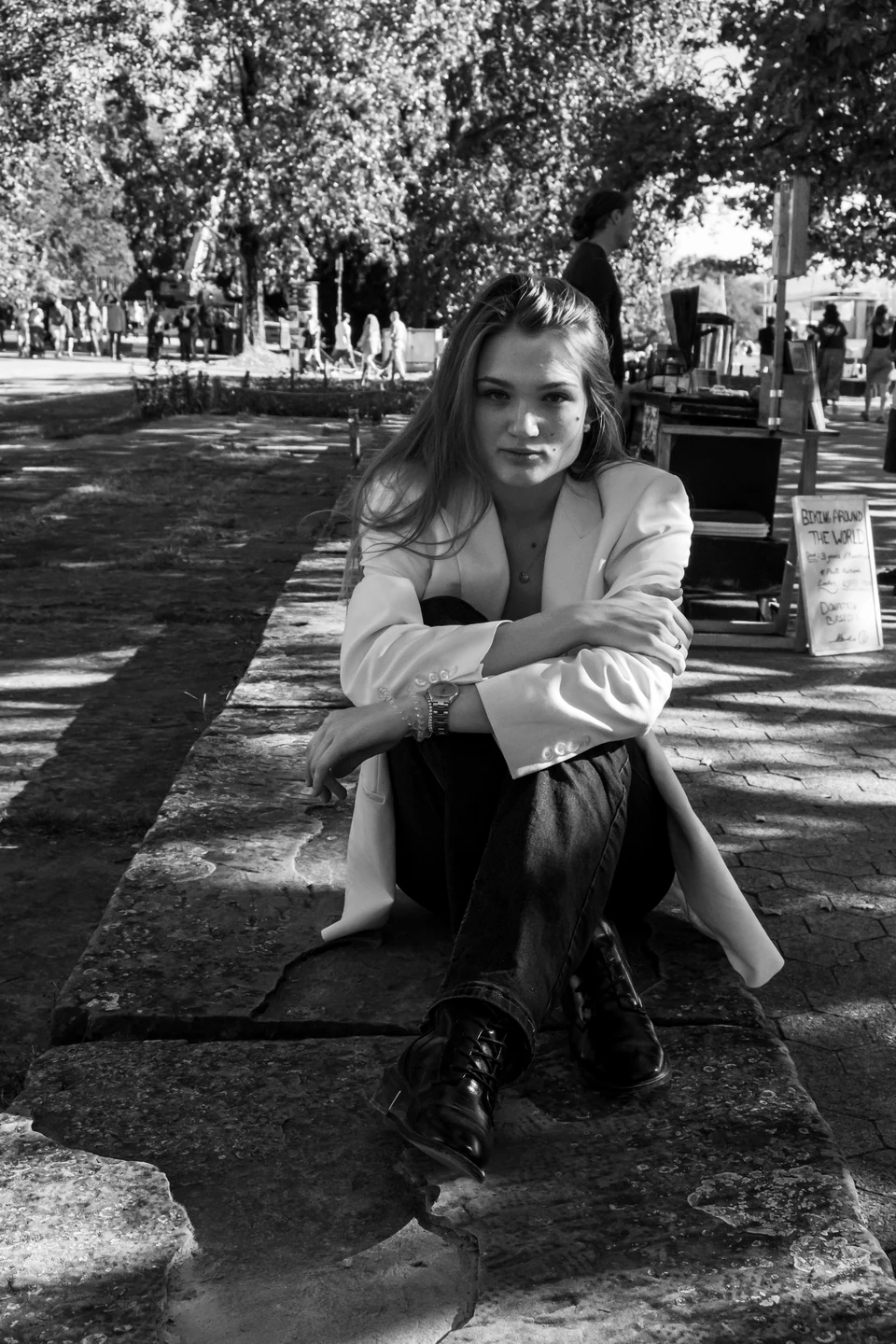 Monochrome seated portrait on a stone wall beneath trees.