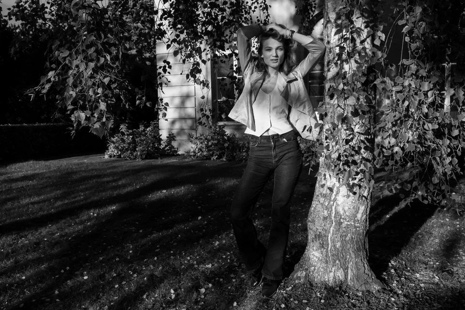 Monochrome environmental portrait beside a tree in dappled light.