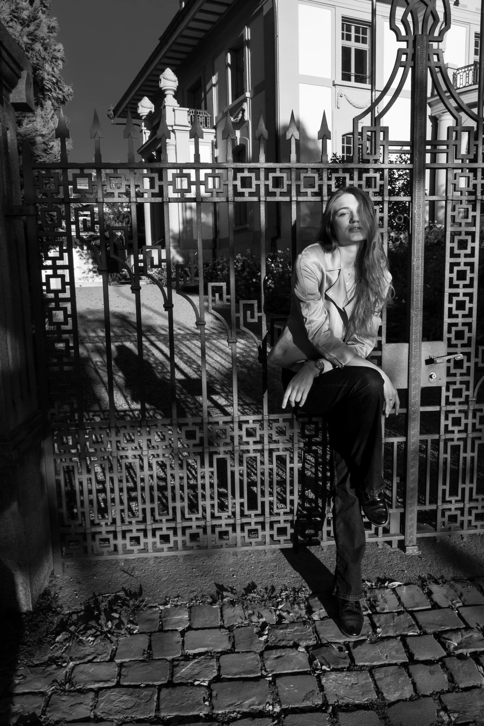Monochrome fashion portrait against an ornate metal gate.