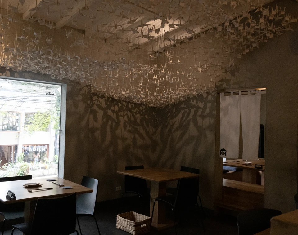 Hanging paper birds and their shadows above a table in a quiet restaurant interior.